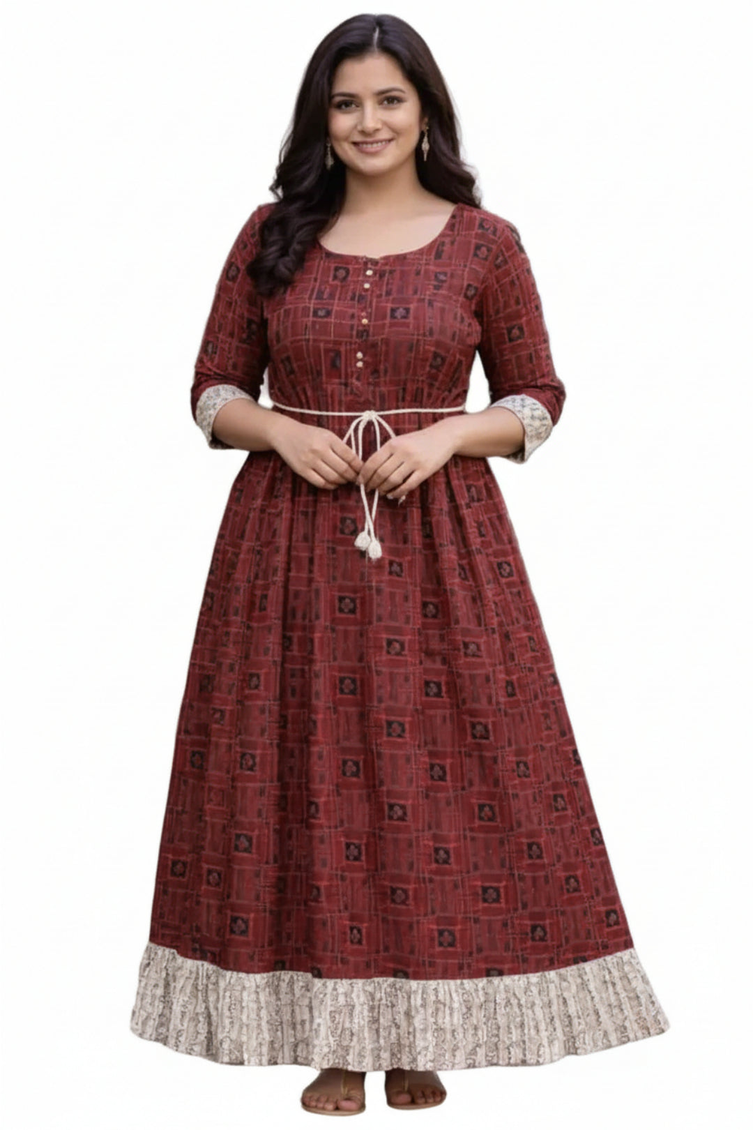 Woman wearing a red patterned dress standing outdoors on a path with greenery.